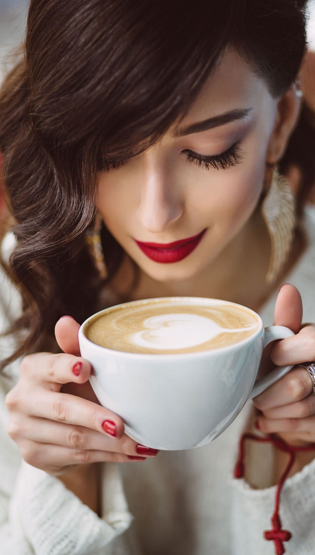 Frau riecht genüsslich an einer Tasse Cappuccino